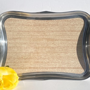 May include: A silver serving tray with a wood-grain design on the bottom. The tray has a wavy edge and a polished silver finish.