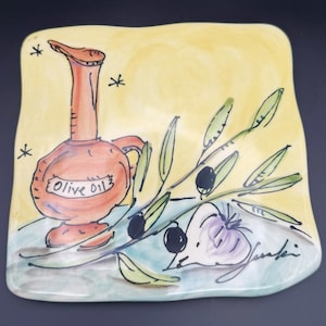 May include: Hand-painted ceramic plate with a whimsical design. Features an orange olive oil bottle labelled "Olive Oil", olive branch with black olives, and a purple garlic bulb. The background is yellow with black star accents.