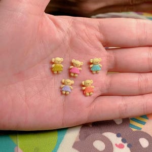 Puede incluir: Cinco ositos de peluche en miniatura tejidos a crochet con vestidos de diferentes colores. Los osos son amarillos, rosas, azules, morados y naranjas.