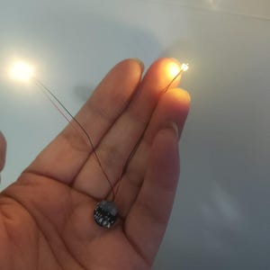 May include: Two small LED lights with wires attached to a round battery pack. The battery pack is black with white text.