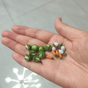 May include: A collection of miniature crocheted vegetables, including green Brussels sprouts, white turnips, and orange carrots.