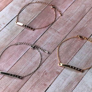 May include: Three gold, silver, and rose gold bracelets with a bar charm engraved with the number "1319".