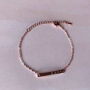 May include: A rose gold chain bracelet with a bar charm engraved with the numbers "1319".