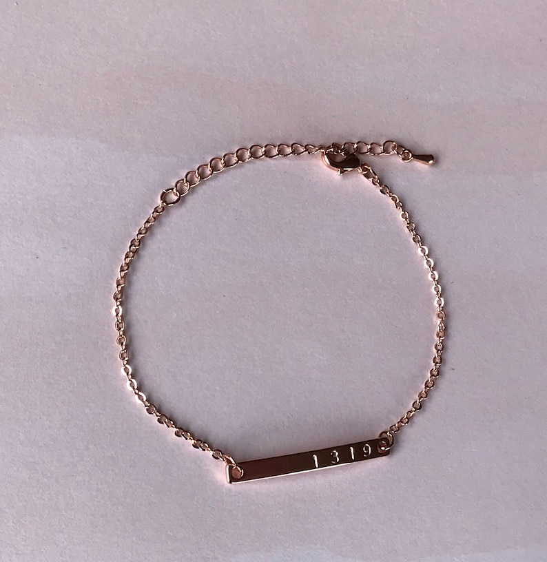 May include: A rose gold chain bracelet with a bar charm engraved with the numbers "1319".