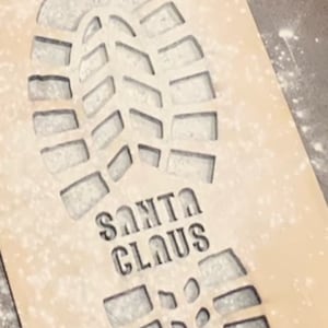 May include: A white wooden stencil of a boot print with the words "SANTA CLAUS" underneath.