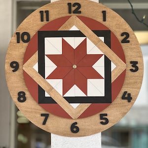 Puede incluir: Un reloj de madera con un diseño de estrella en rojo, blanco y negro. Los números del 1 al 12 se muestran alrededor del borde de la esfera del reloj.