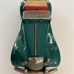 May include: A vintage green toy car with a silver front bumper and headlights. The car has a red interior and a tan top. The toy car is a classic collectible item.