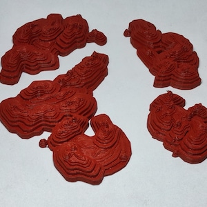 May include: Four red 3D printed models of mountains, each with a different shape and size. The models are made of a layered material, creating a textured surface.