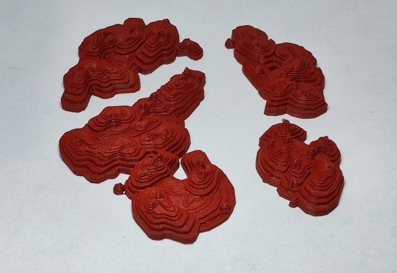 May include: Four red 3D printed models of mountains, each with a different shape and size. The models are made of a layered material, creating a textured surface.