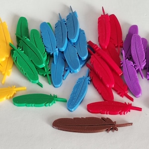 Puede incluir: Una colección de plumas de plástico de colores en amarillo, verde, azul, rojo, morado y marrón. Las plumas están dispuestas en una pila sobre una superficie blanca.