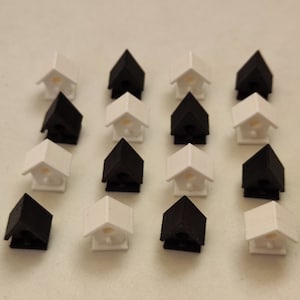 Puede incluir: Una colección de 15 casas de pájaros en miniatura, la mitad pintadas de negro y la mitad pintadas de blanco, dispuestas en un patrón escalonado sobre una superficie blanca.