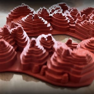 May include: A 3D printed model of a mountain range with a red, layered design.