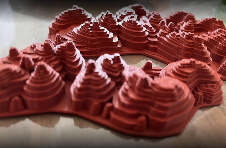 May include: A 3D printed model of a mountain range with a red, layered design.