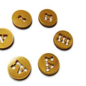 May include: Six gold-colored tokens with different letters and symbols printed on them. The tokens are arranged in a circle on a white background.