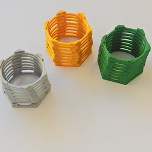 Puede incluir: Tres anillos hexagonales apilados uno encima del otro. El anillo superior es amarillo, el anillo del medio es gris y el anillo inferior es verde.