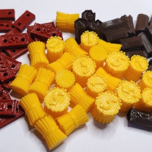Puede incluir: Una colección de piezas de juego impresas en 3D en rojo, amarillo y marrón. Las piezas tienen forma de ladrillos, cilindros y monedas.