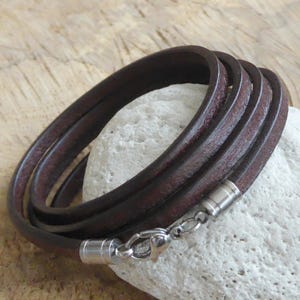 Könnte beinhalten: Ein braunes Lederarmband mit einem silbernen Verschluss. Das Armband besteht aus mehreren Ledersträngen, die um das Handgelenk gewickelt werden.