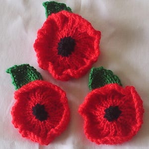 May include: Three handmade red knitted poppy flowers with black centres and green leaves. These decorative floral accents are ideal for crafting or adding a touch of nature to any project.