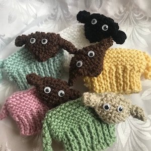 May include: Six knitted sheep plushies in various colours, including brown, black, yellow, green, pink, and beige. Each sheep has a pair of white googly eyes.