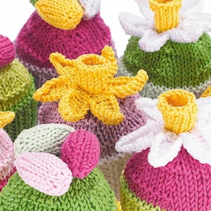 May include: Five knitted flower pot covers in various colors, including pink, green, yellow, and white. Each pot cover features a different flower design, such as a daffodil, a daisy, and a tulip.