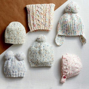 May include: Six white knitted hats with colorful flecks. Some hats have pom-poms and ear flaps. One hat has a button.