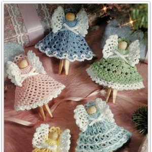 May include: Five crocheted angel ornaments in pink, blue, green, and yellow. Each angel has a white crocheted halo and a white ribbon bow. The angels are attached to wooden clothes pegs.