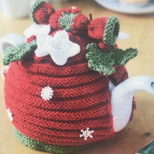 May include: Red knitted teapot cozy with white snowflakes and flowers, green holly leaves, and red berry accents.