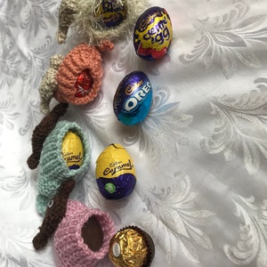 May include: A collection of crocheted Easter bunny figures holding various chocolate eggs, including Cadbury Creme Egg, Cadbury Caramel, and Oreo. There is also a gold-wrapped chocolate truffle.