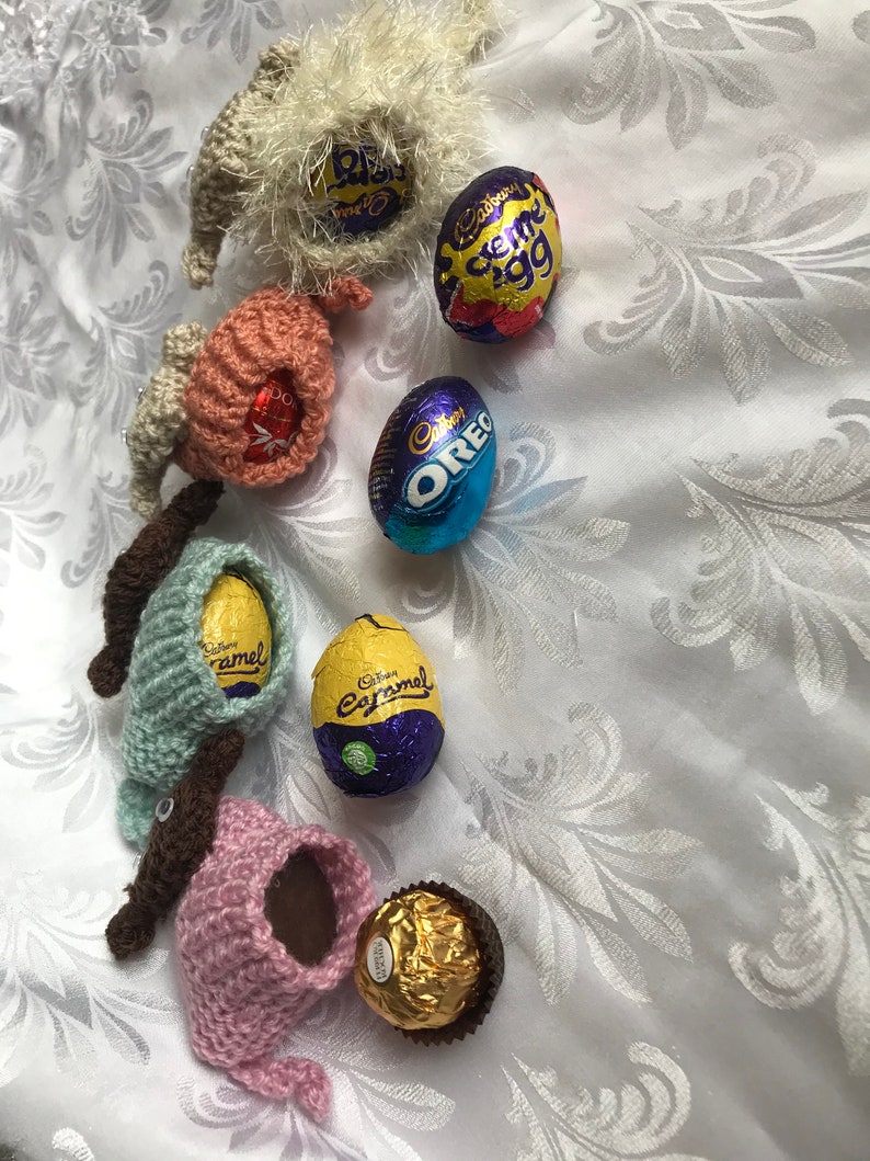 May include: A collection of crocheted Easter bunny figures holding various chocolate eggs, including Cadbury Creme Egg, Cadbury Caramel, and Oreo. There is also a gold-wrapped chocolate truffle.
