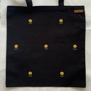 May include: Black canvas tote bag with embroidered yellow sunflowers.