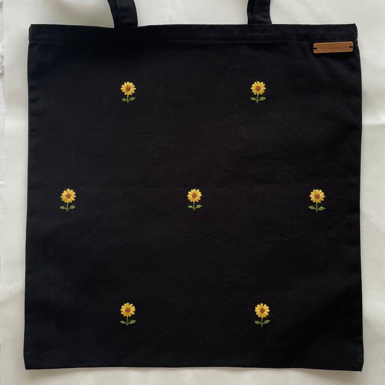 May include: Black canvas tote bag with embroidered yellow sunflowers.