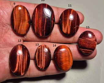 May include: A collection of oval-shaped tiger eye gemstones in various sizes. The stones display a rich, reddish-brown color with striking bands of light and dark hues. The polished surfaces reflect light, highlighting the natural patterns.