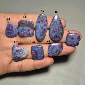 Peut inclure: Collection de huit pierres précieuses polies avec une matrice bleue et des inclusions rouges. Les pierres ont des formes variées, ovales, en goutte et rectangulaires. Les pierres précieuses sont numérotées de 43 à 50.