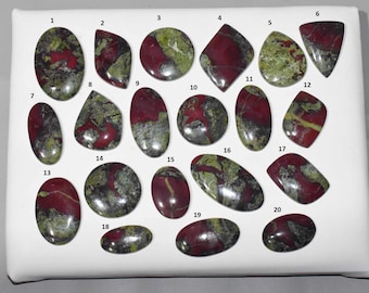 May include: A collection of twenty polished gemstones, each with a unique shape and pattern. The stones feature a mix of deep red and olive green colors, with variations in size and form. The gemstones are displayed on a white surface.