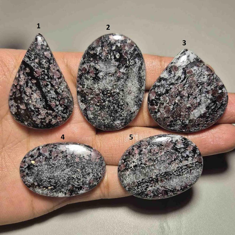 Peut inclure: Cinq pierres pr&eacute;cieuses polies de diff&eacute;rentes formes : goutte d'eau, ovale et arrondie. Les pierres pr&eacute;sentent un motif mouchet&eacute; de teintes noires, blanches et roses. Les pierres pr&eacute;cieuses sont pr&eacute;sent&eacute;es sur un fond clair.