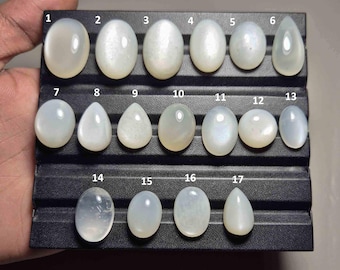 Pode incluir: Uma coleção de dezassete pedras preciosas polidas, em forma oval e de gota, em tons de branco e creme, dispostas numa bandeja preta. As pedras estão numeradas de 1 a 17.