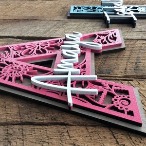 May include: A pink and white wooden sign with the name "Amaya" in white lettering. The sign is decorated with a floral pattern and has a dark brown border.