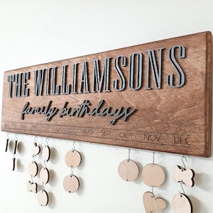 May include: A wooden family birthday calendar with the text "THE WILLIAMSONS family birthdays." The calendar has a dark brown wooden base with silver lettering and wooden tags for each birthday. The months of the year are printed along the bottom.