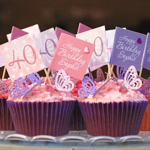Könnte beinhalten: Sechs violette Cupcakes mit rosa Frosting und Streuseln. Jeder Cupcake hat einen dekorativen Topper mit einem Schmetterling und einer Karte mit der Aufschrift "Happy Birthday Sophie" oder "40".