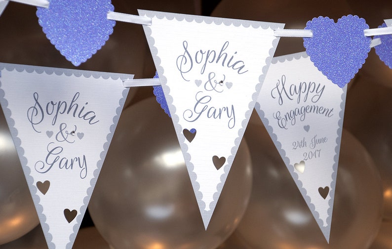 May include: White triangle pennant banner with gray scalloped edges and purple glitter hearts. The banner reads "Sophia & Gary" and "Happy Engagement 24th June 2017".