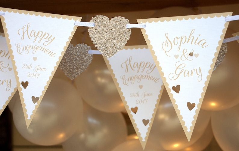 May include: A white and beige engagement banner with the text "Happy Engagement" and the date "24th June 2017". The banner also includes the names "Sophia & Gary" and is decorated with glitter hearts.