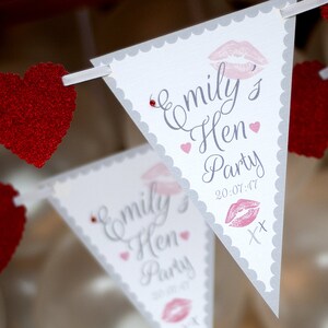 May include: White triangle bunting with gray scalloped edges and red glitter hearts. The bunting has the text "Emily's Hen Party 20-07-47" with a pink lipstick print.