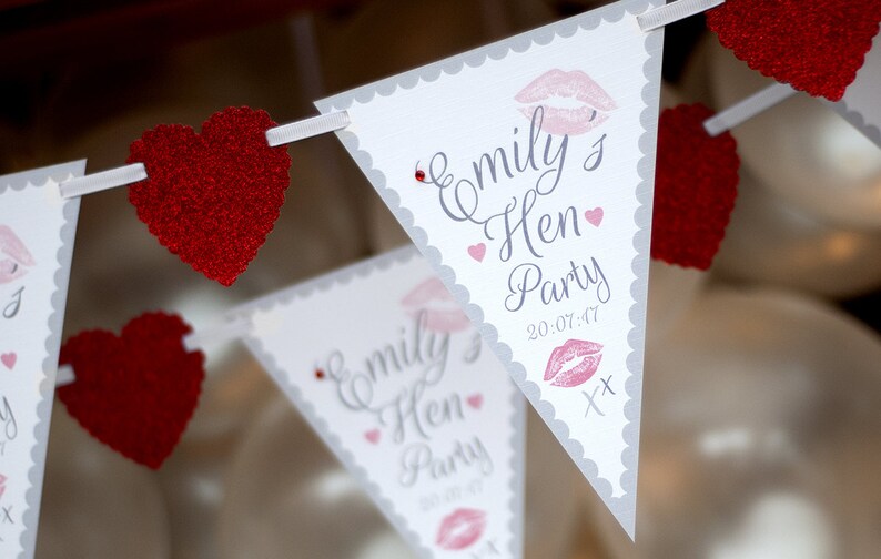 May include: White triangle bunting with gray scalloped edges and red glitter hearts. The bunting has the text "Emily's Hen Party 20-07-47" with a pink lipstick print.