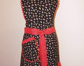May include: A black floral print apron with red polka dot accents. The apron features a scalloped edge, a red polka dot pocket, and a matching waist tie. The bottom hem and trim are red with a scalloped edge.