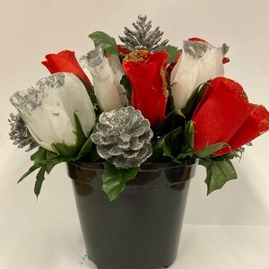 May include: A potted arrangement of artificial red and white roses with glitter accents. The roses are arranged around a silver pine cone and a small silver pine branch.