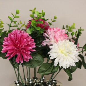 May include: A bouquet of artificial flowers in a silver vase. The flowers are pink, white, and light pink. The flowers are arranged in a cluster and have green leaves.