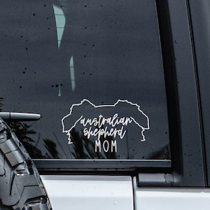 May include: White vinyl decal on a black car window. The decal is a silhouette of an Australian Shepherd with the text "Australian Shepherd Mom".
