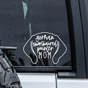 May include: White vinyl decal for a car window. The decal is shaped like a dog's head and says "German Shorthaired Pointer Mom".