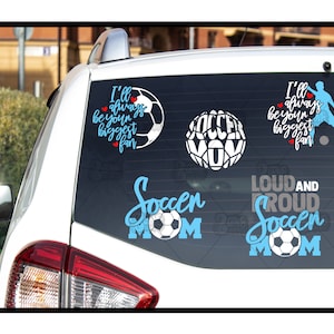 May include: A white car with a black rear window. The window has several blue and white decals with soccer-themed text and images. The text includes "I'll always be your biggest fan", "Soccer Mom", and "Loud and Proud Soccer Mom".