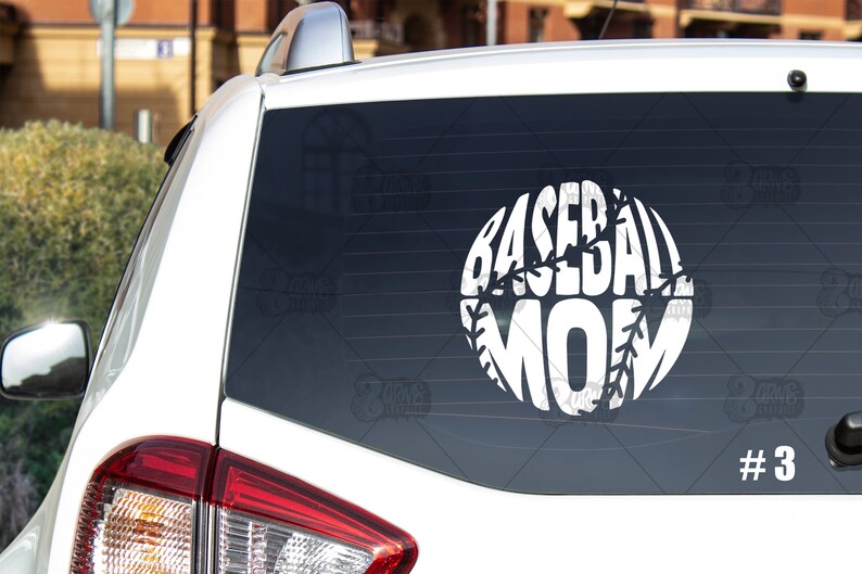 May include: White car with a white vinyl decal on the back window. The decal is a baseball with the word "MOM" inside of it. The number "#3" is printed on the lower right corner of the window.